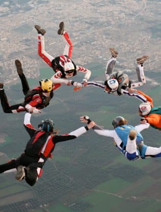 Skydivers holding hands in a circle formation in freefall above the plain